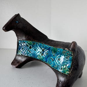 Puede incluir: Figura de caballo de cerámica marrón oscuro con una banda estampada turquesa y verde en la espalda. El caballo tiene un diseño estilizado y un acabado brillante. La figura es una pieza de arte decorativa.