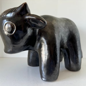 May include: Black ceramic sculpture of a stylised calf. The sculpture has a glossy finish and is standing on a white surface.