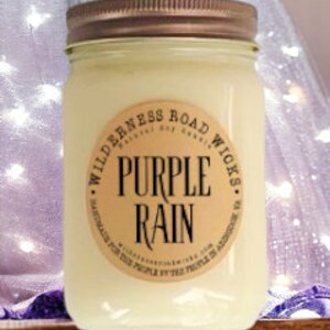May include: A jar candle with a metal lid and a label that reads "Purple Rain." The label also includes the text "Wilderness Road Wicks" and "Handmade for the people by the people in Abingdon, VA."