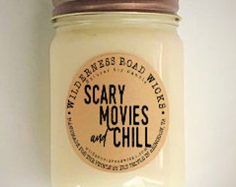 May include: A white candle in a clear glass jar with a brown lid. The label reads "Wilderness Road Wicks" and "Scary Movies and Chill".