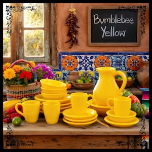 May include: A vibrant display of yellow ceramic tableware, including mugs, saucers, bowls, and a pitcher, arranged on a wooden surface. The backdrop features a chalkboard with "Bumblebee Yellow" written on it, along with a basket of flowers and colorful tiles.
