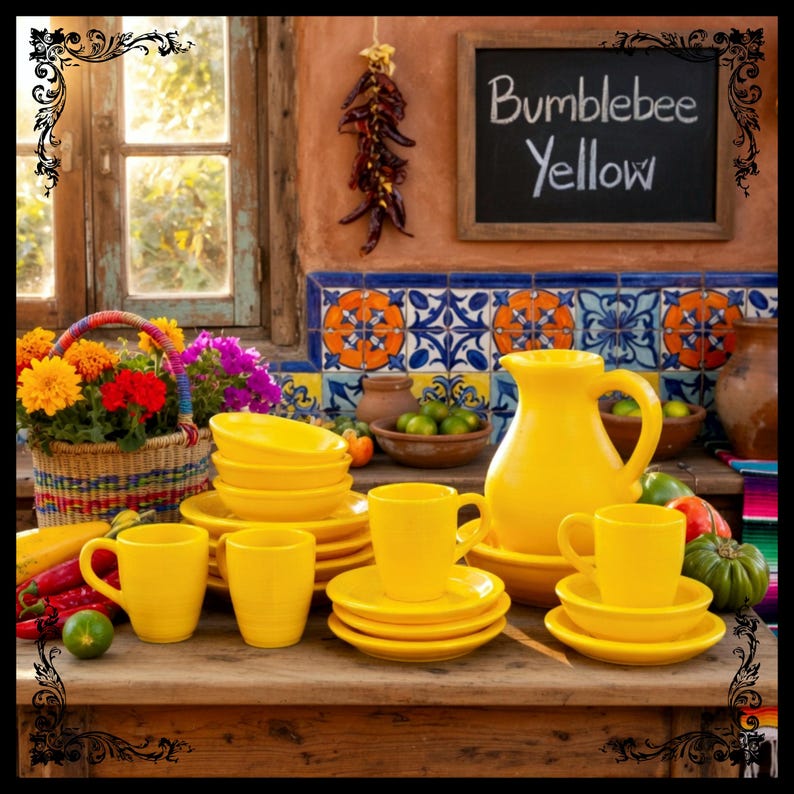 May include: A vibrant display of yellow ceramic tableware, including mugs, saucers, bowls, and a pitcher, arranged on a wooden surface. The backdrop features a chalkboard with "Bumblebee Yellow" written on it, along with a basket of flowers and colorful tiles.