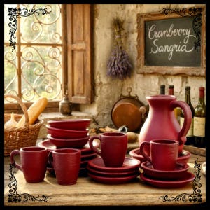 May include: A rustic kitchen scene featuring a collection of red ceramic tableware. The set includes mugs, saucers, and bowls, alongside a large pitcher. A chalkboard sign reads "Cranberry Sangria". A basket of bread and garlic is visible.