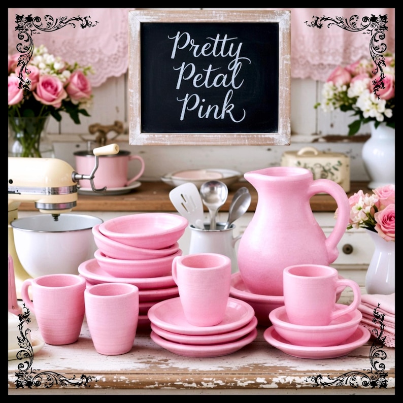 May include: A collection of pink ceramic dishware, including cups, saucers, bowls, and a pitcher, arranged on a distressed white surface. A chalkboard sign with the text "Pretty Petal Pink" is in the background, along with floral arrangements and a stand mixer.