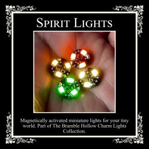 May include: Four small circular circuit boards labeled SPIRIT LIGHTS, each featuring multiple surface-mounted LEDs. Three units emit a warm white glow, while one unit emits a bright green light. These magnetically activated miniature lights are part of The Bramble Hollow Charm Lights Collection.
