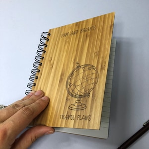 May include: A brown bamboo notebook with a spiral binding. The front cover has a globe design and the text "Pam and Brian's Travel Plans".