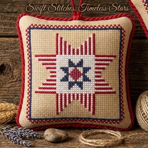 May include: Square, cross-stitched pillow with a starburst design in red, white, and blue. The pillow has a beige background, a red border, and a red hanging loop. The text "Swift Stitches, Timeless Stars" is at the top.