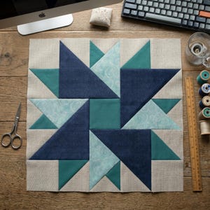 May include: A handcrafted quilt block featuring a starburst design. The block is composed of various shades of blue and teal fabric, with a neutral linen-colored background. The design includes triangles and squares, showcasing a geometric pattern. The block is likely for a quilting project.