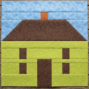 Könnte beinhalten: Ein quadratischer Quiltblock mit einem Hausmotiv. Das Haus hat ein braunes Dach mit einem orangefarbenen Schornstein, einen hellgrünen Körper sowie eine braune mittige Tür und zwei braune Fenster. Der Hintergrund ist hellblauer Stoff.