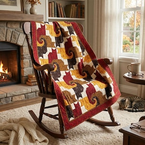 May include: A quilt featuring a repeating pattern of stylized cats in shades of red, gold, and dark brown. The quilt has a solid red border and is draped over a dark wooden rocking chair. The fabric displays intricate swirling textures.