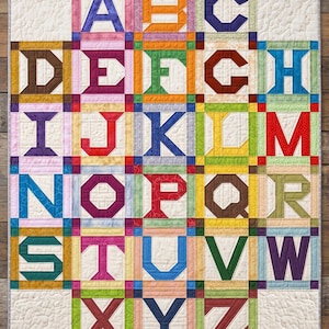 May include: A vibrant alphabet quilt showcasing each letter in a distinct block. The quilt uses a range of colours, such as blue, red, green, and yellow, with each letter outlined in a contrasting shade. The design is a patchwork style.