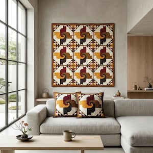 May include: A geometric quilt and two matching throw pillows. The quilt and pillows feature a repeating pattern of abstract shapes in shades of brown, yellow, and burgundy, set against a cream background. The quilt is displayed above a light gray sofa.