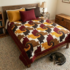 May include: A quilt featuring a repeating pattern of stylized cat shapes in shades of mustard yellow, dark brown, and deep red, arranged on a cream-colored background. The quilt covers a wooden bed frame with a mustard yellow pillow and a dark red pillow.