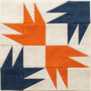 Könnte beinhalten: Ein quadratischer Quiltblock mit einem Bärenpfotenmuster aus Stoffstücken. Das Design besteht aus zwei orangefarbenen und zwei dunkelblauen Pfotenformen auf einem hellen, cremefarbenen Hintergrund mit einer dezenten, gesprenkelten Textur.