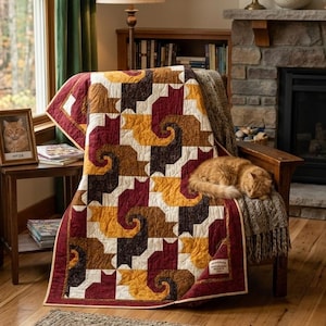 May include: A quilt featuring a repeating geometric pattern of stylized cats in shades of burgundy, mustard yellow, dark brown, and cream. The fabric has a subtle texture, and a small rectangular label is stitched onto the bottom right corner.