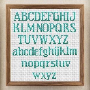 Könnte beinhalten: Kreuzstich-Alphabet-Sampler in einem Holzrahmen. Die Buchstaben sind in türkisfarbenem Garn auf weißem Hintergrund gestickt. Der Sampler enthält Groß- und Kleinbuchstaben.