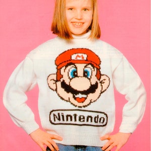 May include: White knit sweater featuring a large Mario graphic with a red hat and the word "Nintendo" below. The sweater is worn with blue jeans. The image is set against a pink background.