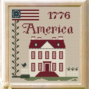 Op de afbeelding: Borduurpatroon met een wit huis met een rood dak en rode versieringen, een blauwe vogel en een wit hek. De tekst "1776 America" is boven het huis geborduurd.