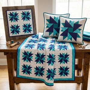 May include: A rustic wooden table displays a collection of home decor items. A framed quilt, two throw pillows, and a table runner feature a geometric starburst pattern in shades of blue and teal on a white background. Sewing notions are also visible.
