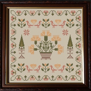 Puede incluir: Un bordado de punto de cruz enmarcado que presenta un diseño floral con una cesta de flores en el centro. Las flores son amarillas, naranjas y verdes, y la cesta es marrón. El borde del bordado es un patrón repetido de hojas verdes y flores rosas.