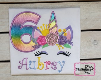 May include: A white t-shirt with a rainbow glitter number six, a unicorn head with a crown, flowers, and eyelashes, and the name Aubrey in rainbow letters.