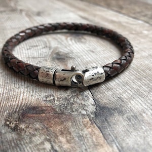 May include: A brown leather braided bracelet with a silver clasp. The clasp has a textured finish.