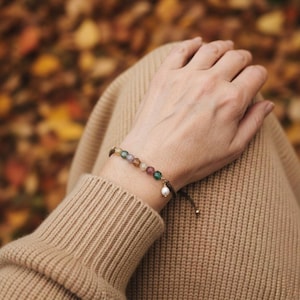 Pulsera con dijes de ágata y perla, cierre de cordón ajustable, ideal como regalo.