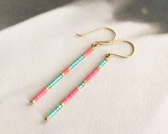 May include: A pair of long, gold dangle earrings with pink and turquoise beads. The earrings are made with small, round beads that are strung together to create a long, thin line.