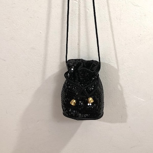 May include: A small black sequined drawstring bag with a long black strap and gold accents.