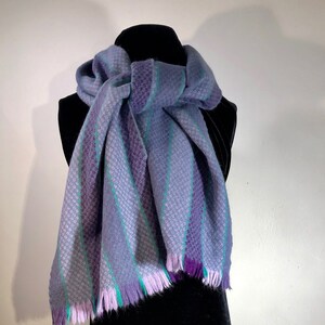 A purple, lilac and grey striped soft, warm scarf nicely accented with thin strips of contrasting greenish turquoise.