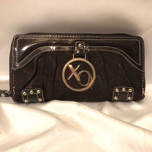 XOXO - Una cartera de tela XOXO monograma en tonócobre de cobre en tonizado marrón de chocolate oscuro con ribete marrón brillante y un logotipo XOXO de metal dorado.