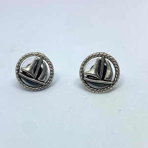 May include: A pair of silver earrings with a sailboat design. The sailboats are surrounded by a rope-like border.