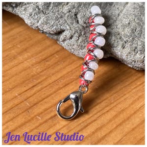 May include: A silver charm with a silver chain and alternating white and coral colored beads. The charm has a silver lobster clasp.
