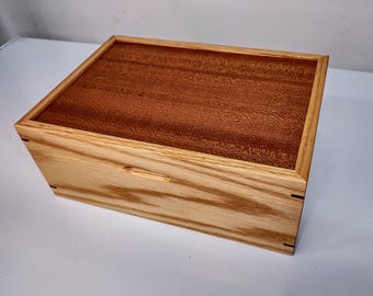 May include: A wooden box with a light brown exterior and a dark brown lid. The box has a simple design with a subtle grain pattern.