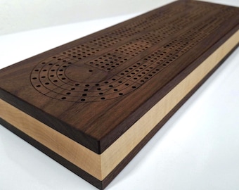 May include: A rectangular cribbage board made of dark brown wood with a light brown border. The board has a series of drilled holes for pegs and a curved track. A classic game for family fun.