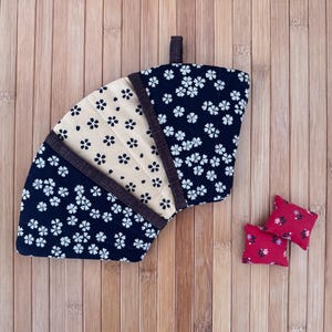 May include: A fan-shaped, quilted fabric item with a dark blue floral pattern and a tan center section. Two small red pillows with floral designs are also present. The items are on a wooden surface.