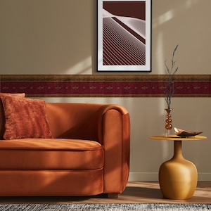 Maroon and gold Napoleonic Bee wallpaper border styled in a living room with tan walls, a rust velvet sofa, and modern gold accent decor.