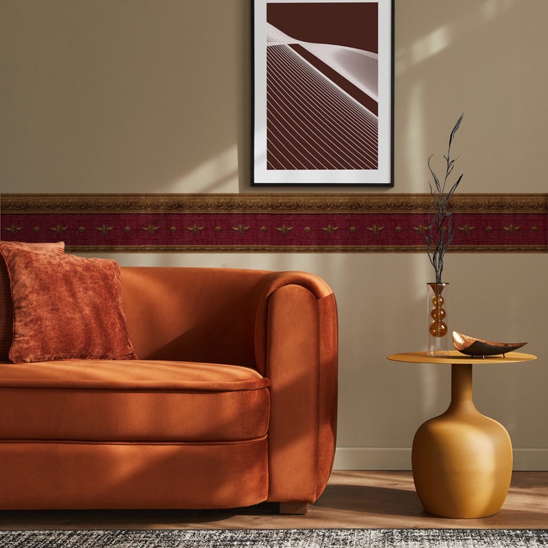 Maroon and gold Napoleonic Bee wallpaper border styled in a living room with tan walls, a rust velvet sofa, and modern gold accent decor.
