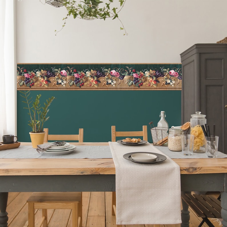 Puede incluir: Un comedor con una pared verde azulada y un borde de papel tapiz floral. Una mesa de madera con un mantel blanco y dos sillas est&aacute; puesta con platos y vasos.