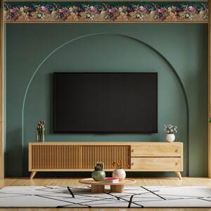 Puede incluir: Un mueble de TV de madera con dos cajones y un televisor negro en la parte superior. El mueble est&aacute; delante de una pared verde azulada con un borde de papel tapiz floral. Hay una peque&ntilde;a planta en maceta en el mueble y una mesa de caf&eacute; con un libro y dos plantas en maceta.