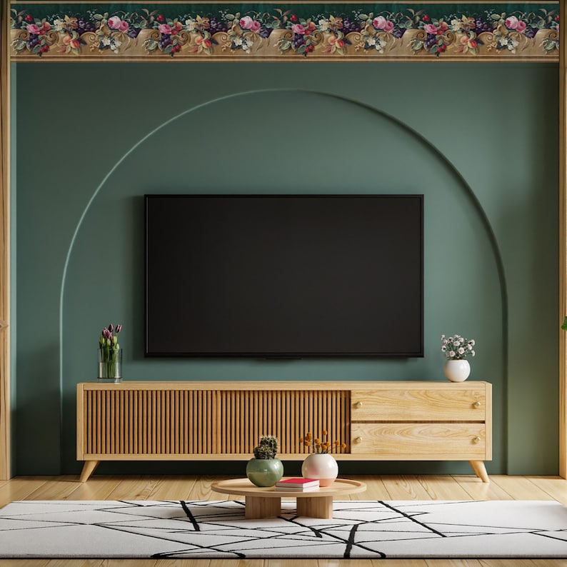 Puede incluir: Un mueble de TV de madera con dos cajones y un televisor negro en la parte superior. El mueble est&aacute; delante de una pared verde azulada con un borde de papel tapiz floral. Hay una peque&ntilde;a planta en maceta en el mueble y una mesa de caf&eacute; con un libro y dos plantas en maceta.