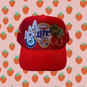 May include: Red trucker hat with a variety of patches, including a number "44", a "Miller Lite" logo, a smiley face, and a cherry.