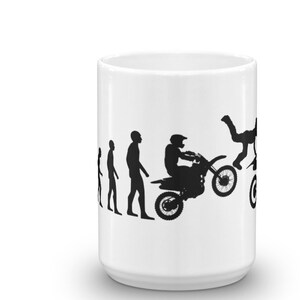 May include: White ceramic mug with a black silhouette design of the evolution of man, ending with a man riding a dirt bike and doing a backflip.