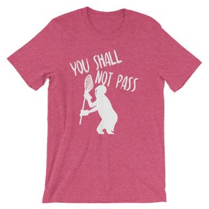 May include: A pink t-shirt with the text "You Shall Not Pass" in white lettering. A white silhouette of a person holding a lacrosse stick is below the text.