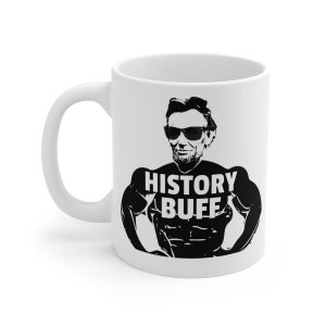 May include: White ceramic coffee mug with a black and white illustration of Abraham Lincoln wearing sunglasses and a muscular body. The text "HISTORY BUFF" is printed on the mug.