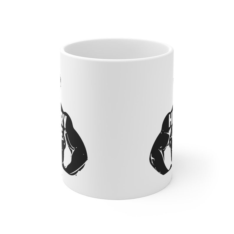 May include: White ceramic mug with a black silhouette of a bicep flexing with the text "Heavy is the head that wears the crown" on each side.