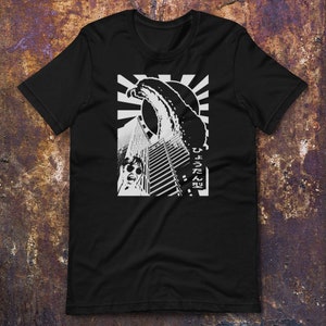 May include: Black t-shirt featuring a white graphic design of a wave crashing over a city skyline. The text "ひろうてん" is printed on the shirt.
