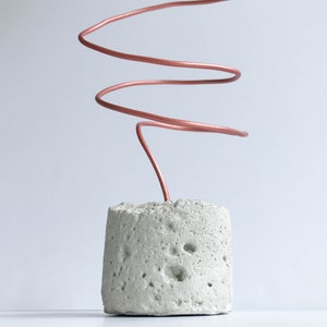 May include: A concrete base with a copper wire coiled and extending upwards. The wire is a light copper color.