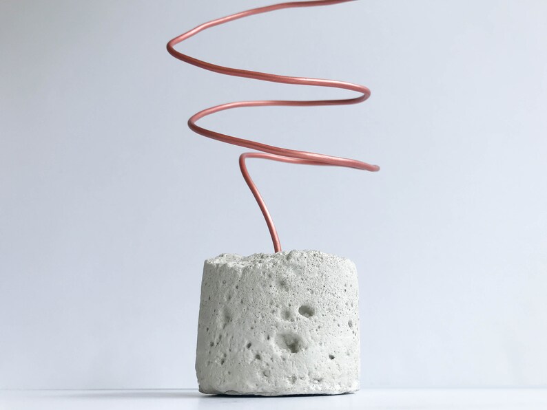 May include: A concrete base with a copper wire coiled and extending upwards. The wire is a light copper color.