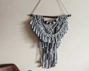 Tapiz de macramé gris claro para pared con rama de madera y cuentas.